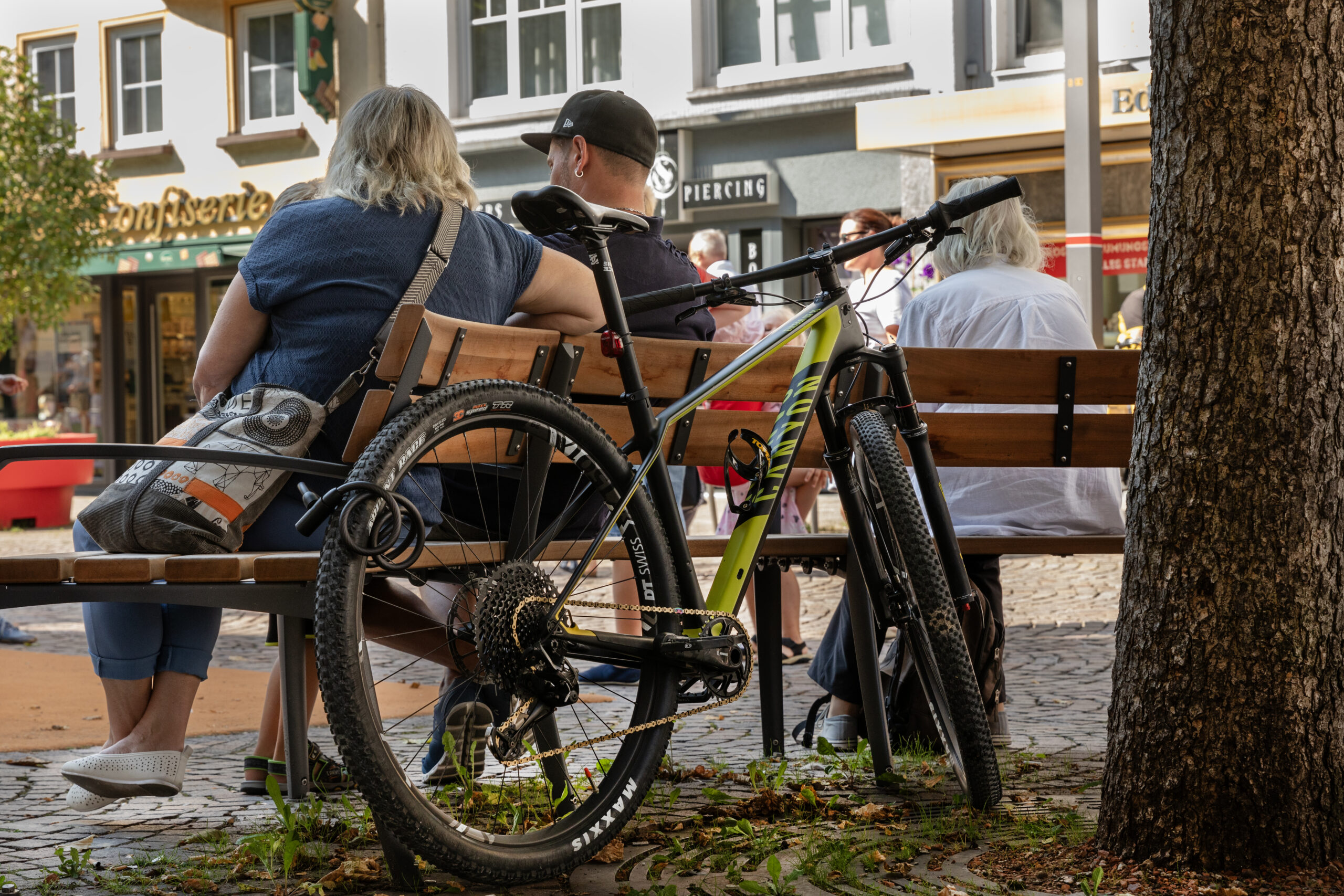 Fotografie eines Fahrrads angeschlossen an einer Bank auf der zwei Personen sitzen