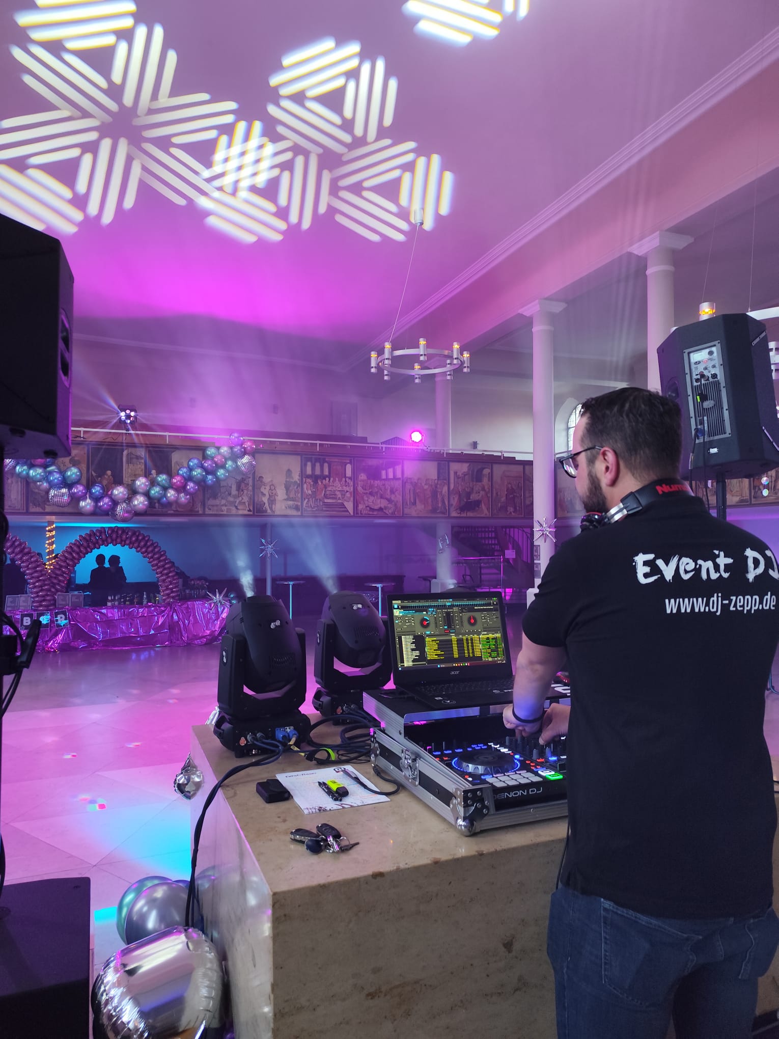 Ein DJ von hinten mit Blick auf eine leere, aber dekorierte Tanzfläche.